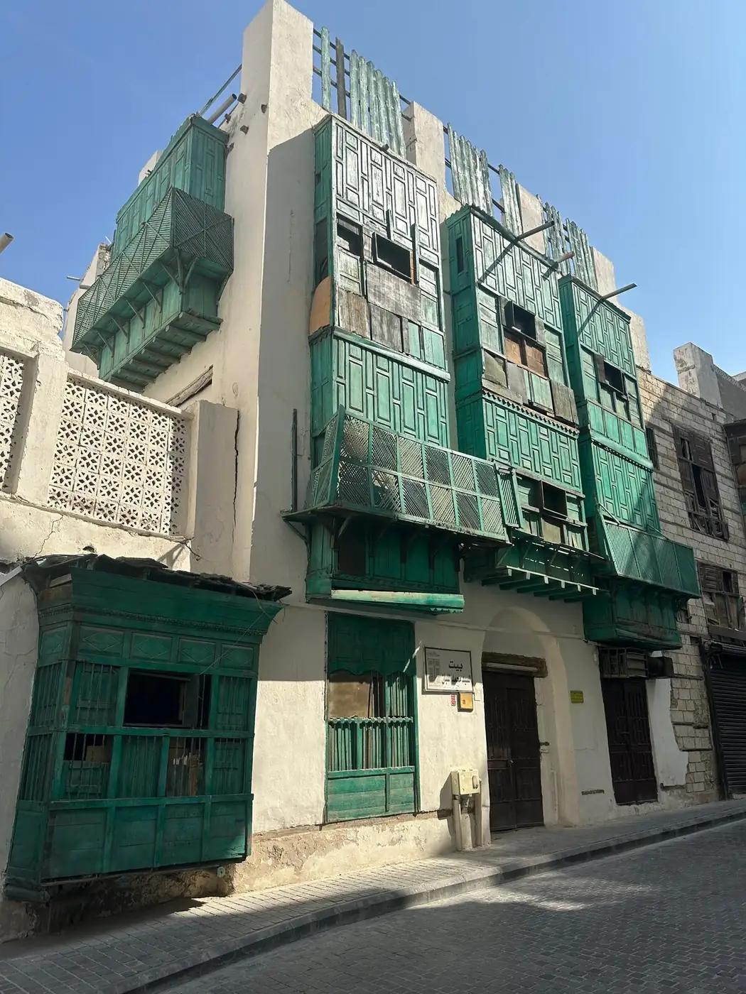 Coral-stone merchant house in Al-Balad with full green rawasheen lattice balconies